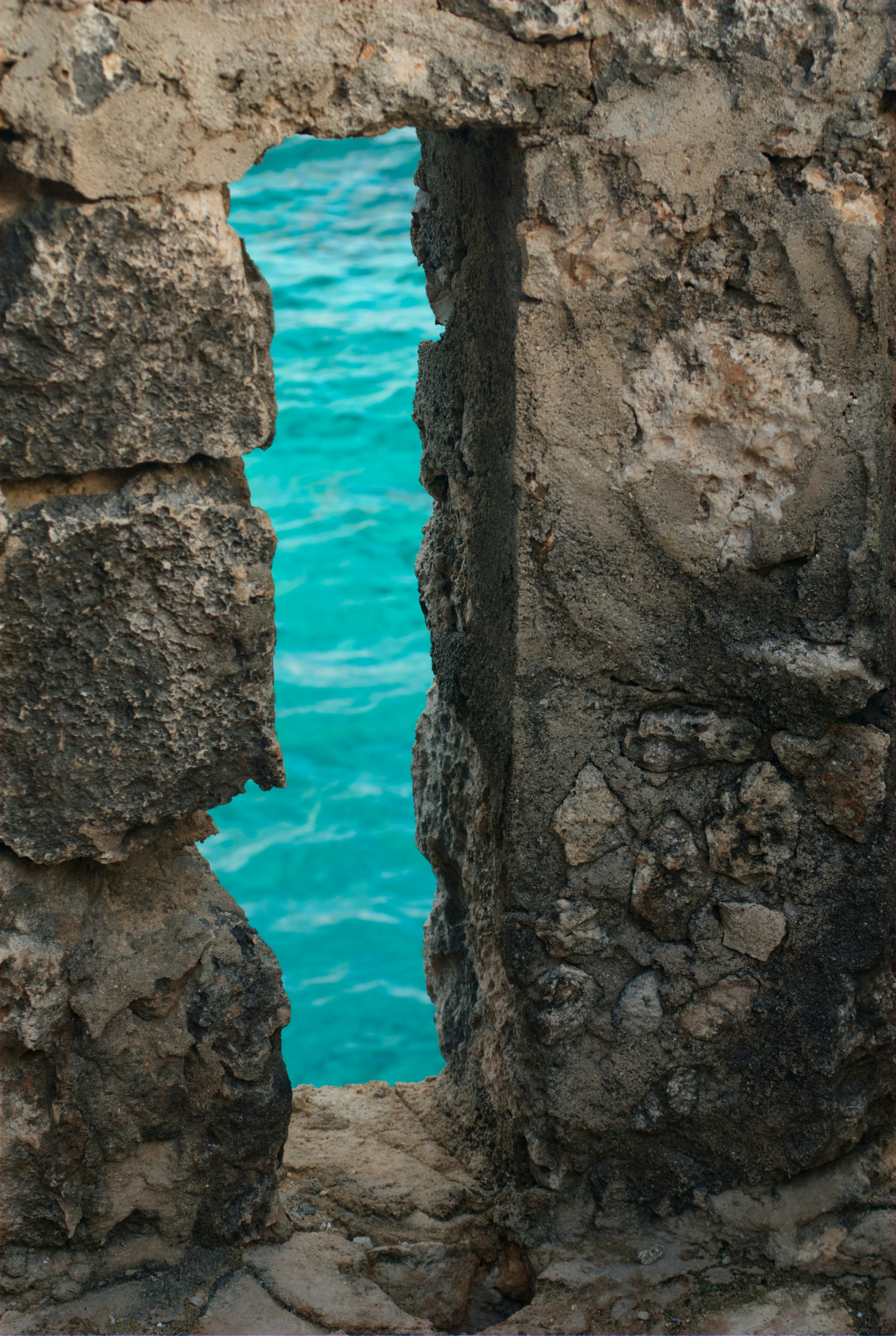 A window in a stone wall with a blue body of water in the background